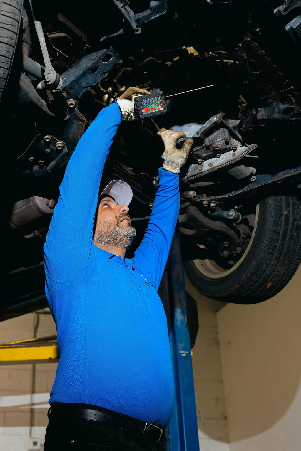 Technician examining the underside of a vehicle raised on a workshop lift